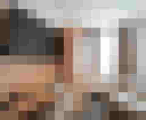 kleines Hotelzimmer mit Fernseher, Schreibtisch, Holzschrank und hellgrauem Sofa